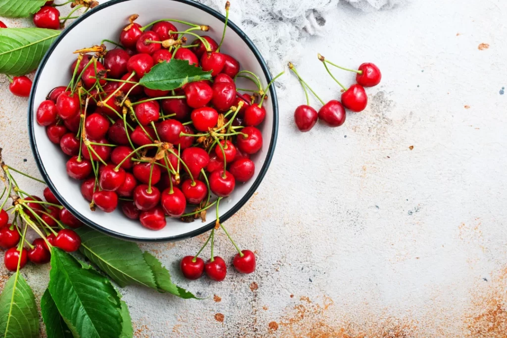 Red cherries in a bowl with green leaves.