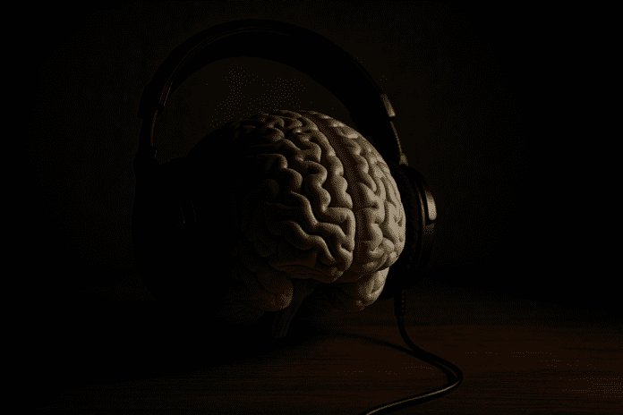 A realistic brain model rests on a wooden table, encased in large over-ear headphones and dramatically lit from the left, casting deep shadows across a moody background. The image evokes the science of calm study music and its role in supporting mental clarity and long-term cognitive health.